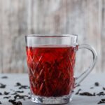Tea with dried black tea in a glass cup on plaster and grungy background, side view.